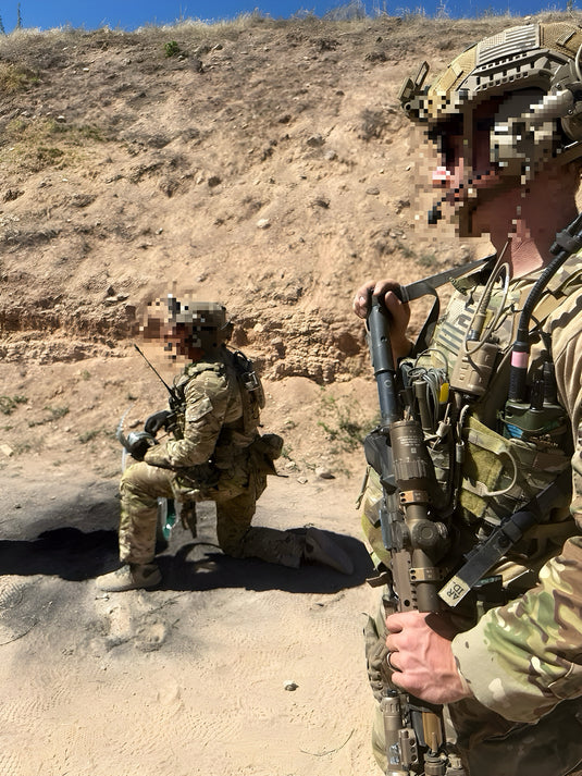 Two soldiers in military gear on a rocky terrain with a clear sky.